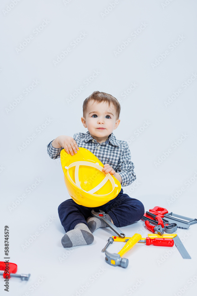 A little boy in a shirt with a helmet and a toy tool. White background. Toy construction tool for children A little boy in a shirt with a helmet and a toy tool. White background. Toy construction tool for children