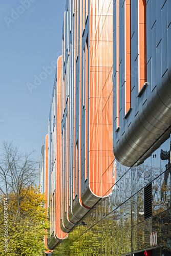 Kolorowy detal na elewacje obiektu, budynku. Materiał z pionowych aluminiowych i pomarańczowych paneli. Nowoczesny budynek. Okna i odbicia