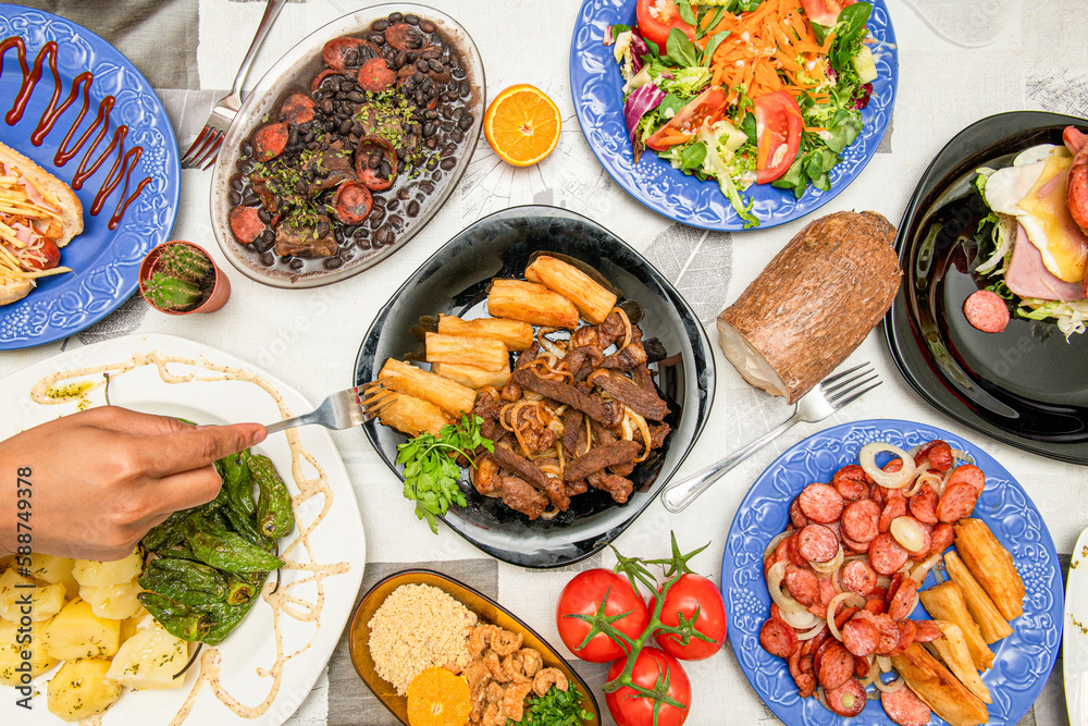 Hand with fork cutting food from exposed plates of typical Brazilian food