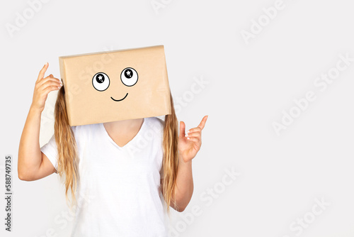 Mujer con caja de cartón en la cabeza y con un gesto con los dedos de la mano señalando hacia arriba sobre fondo gris claro liso y aislado. Vista de frente y de cerca. Copy space 