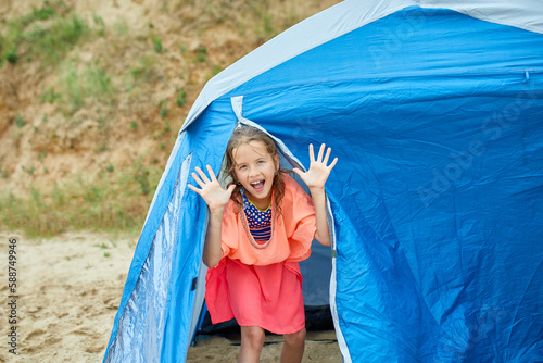 A happy girl child looks out of a tent on the seashore