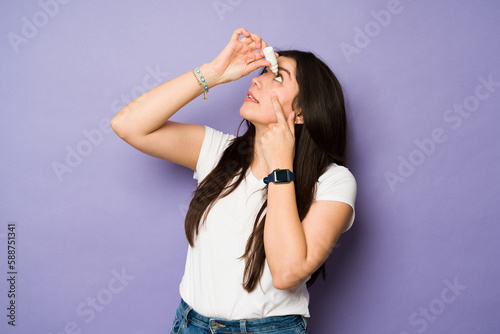 Sick young woman using eye drops photo