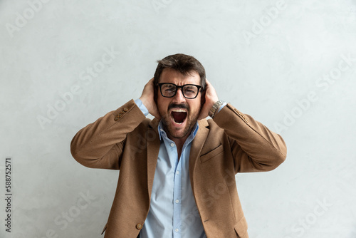 Young business man office worker covered his ears with his hands and shouts because he can't stand the noise and commotion in the office at the workplace