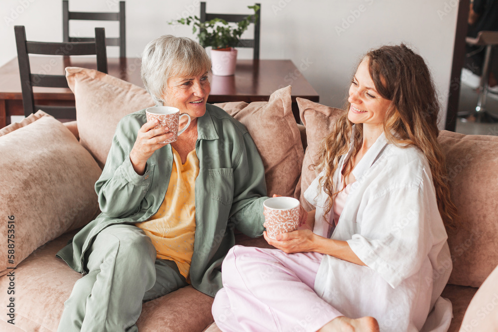 Happy adult daughter and senior mother having fun enjoying talk sit on sofa at home Happy adult daughter and senior mother having fun enjoying talk sit on sofa at home