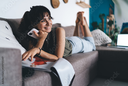 Εκτύπωση καμβά Cheerful woman with smartphone and magazine relaxing on sofa