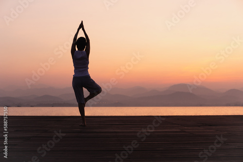 Full length rear view of woman standing on one leg while doing yoga at sunrise.