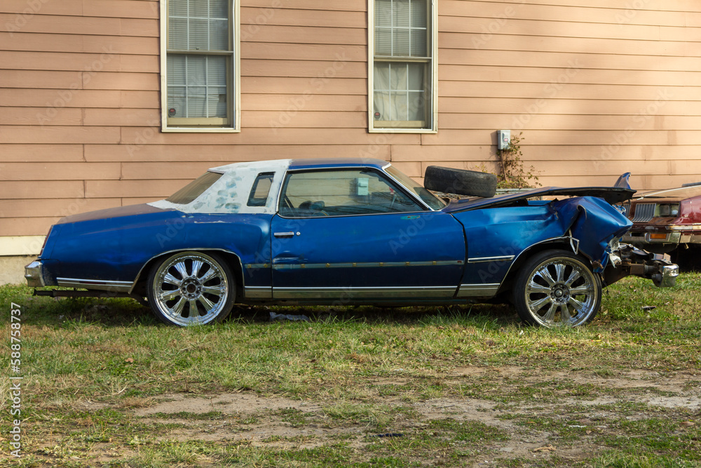 Smashed up blue luxury car sitting forgotten on side of house