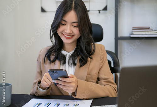 Head shot of pleasant asian girl holding smartphone  reading good news sms  using mobile applications at workplace. Happy young asian business woman enjoying spending time in social network.