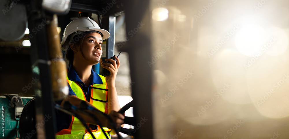 Indian woman worker driving a forklift and using a walkie-talkie at warehouse factory container. communication radio. Inventory and wholesale concept - obrazy, fototapety, plakaty 
