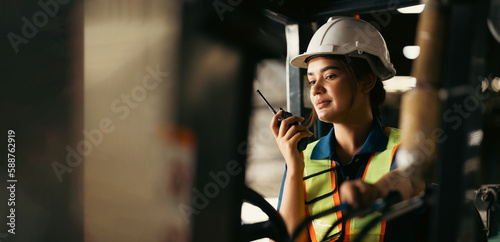 Indian woman worker driving a forklift and using a walkie-talkie at warehouse factory container. communication radio. Inventory and wholesale concept photo