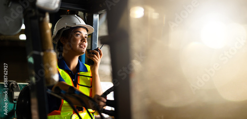 Indian woman worker driving a forklift and using a walkie-talkie at warehouse factory container Fototapet
