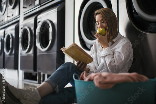 Slika na platnu Young woman reading a book, waiting in a laundry room.