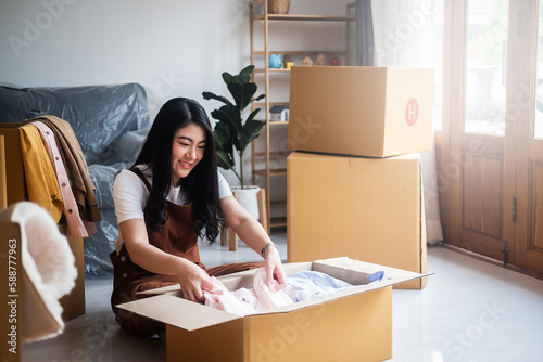 New house, asian woman put the clothes in the box while feeling proud and excited about buying a house with a mortgage loan. Young asian woman first time buyers unpacking in dream home or apartment