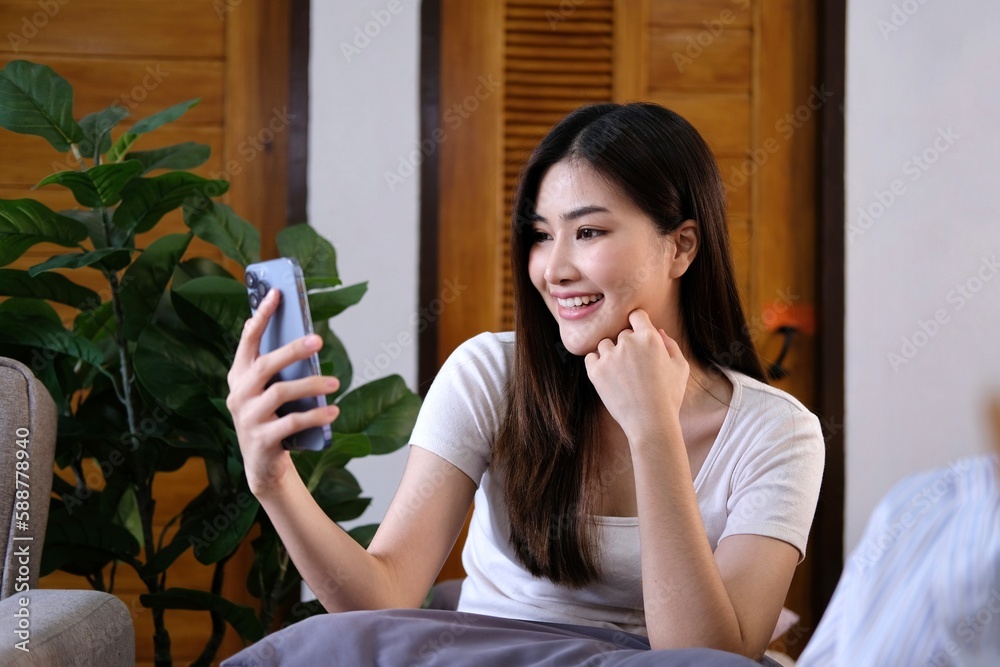 Happy relaxed young woman sitting on couch using cell phone, smiling lady laughing holding smartphone, looking at cellphone enjoying doing online ecommerce shopping in mobile apps or watching videos. Happy relaxed young woman sitting on couch using cell phone, smiling lady laughing holding smartphone, looking at cellphone enjoying doing online ecommerce shopping in mobile apps or watching videos.