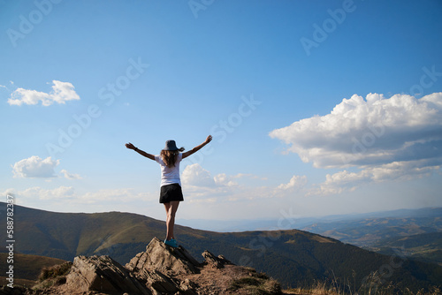 Young women standing on rock on top of the mountain. Feeling happy and free. Natural landscape in summer. Sunny rural scenery. Nature protection concept. Breathtaking mountain view.On top of the world