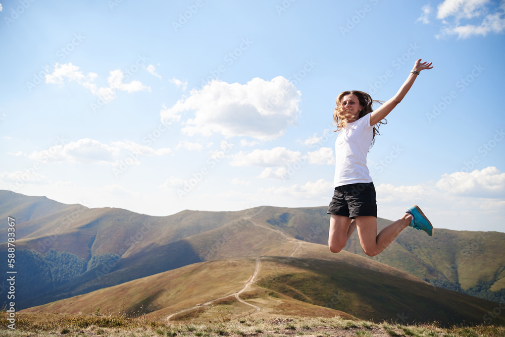 Young woman jumping on top of the mountain. Feeling happy and free. Natural landscape in summer. Sunny rural scenery. Nature protection concept. Breathtaking mountain view.. On top of the world Young woman jumping on top of the mountain. Feeling happy and free. Natural landscape in summer. Sunny rural scenery. Nature protection concept. Breathtaking mountain view.. On top of the world