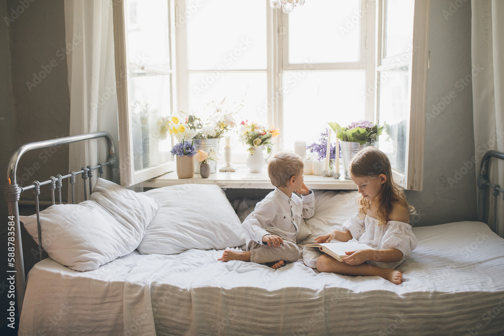 Cute boy and girl sitting on bed reading book together near window. Cute boy and girl sitting on bed reading book together near window.