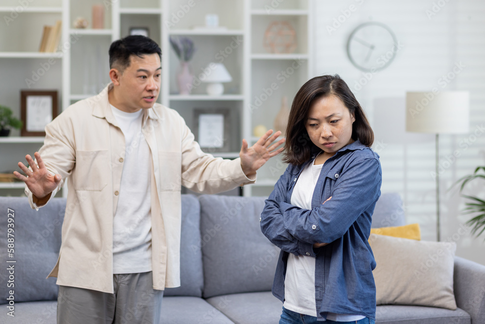 Family quarrel, asian couple man and woman yelling at each other, family conflict, asians at home standing angry in living room. Family quarrel, asian couple man and woman yelling at each other, family conflict, asians at home standing angry in living room.