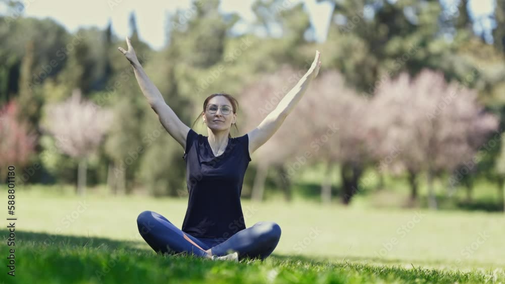 Smiling adult woman in glasses sits in the lotus position and stretching her arms Smiling adult woman in glasses sits in the lotus position and stretching her arms