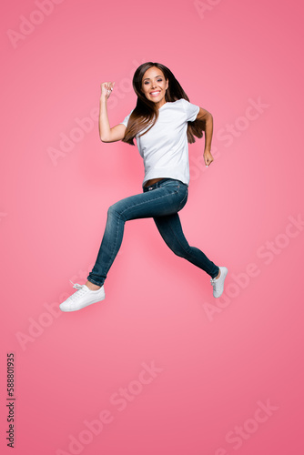 Full lenght portrait of brown-haired gorgeous attractive nice lovely excited smiling young lady wearing jeans and white t-shirt, flying showing motion running hurry over grey background, isolated