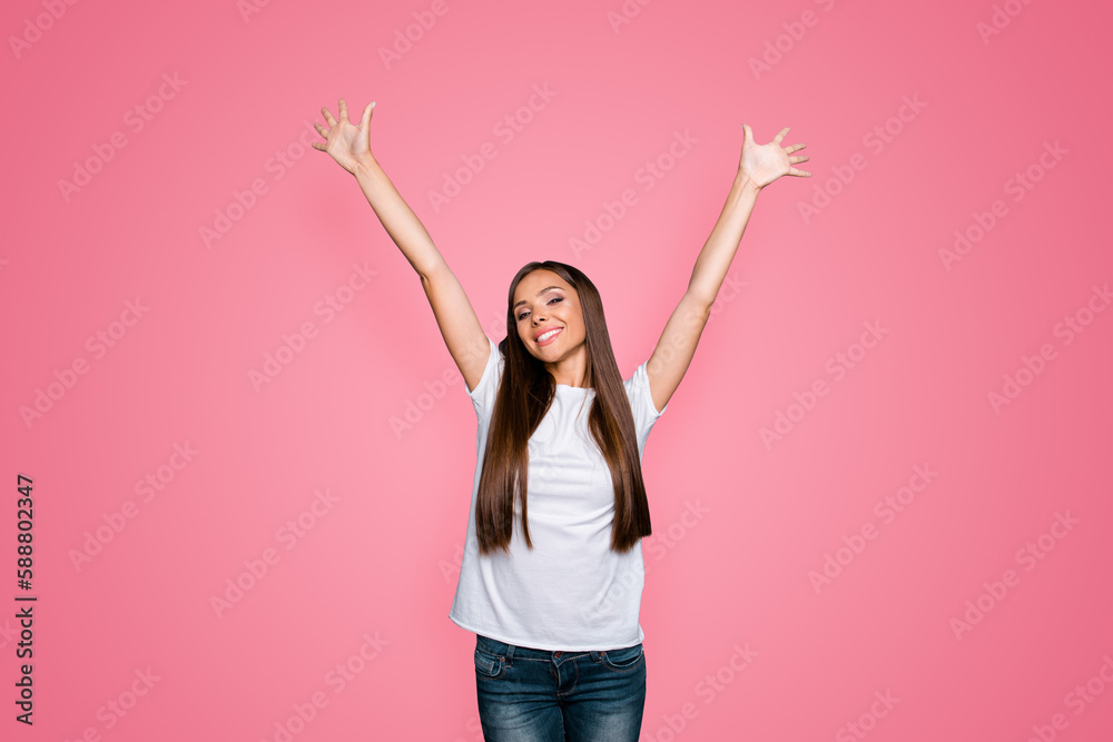 Portrait of brown-haired gorgeous attractive nice excited smiling young lady with long straight hair wearing jeans and white t-shirt, raising hands up over grey background, isolated