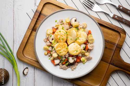 Stir fried egg tofu and chicken in oyster sauce with corn, carrot and shiitake in white dish on wooden table.