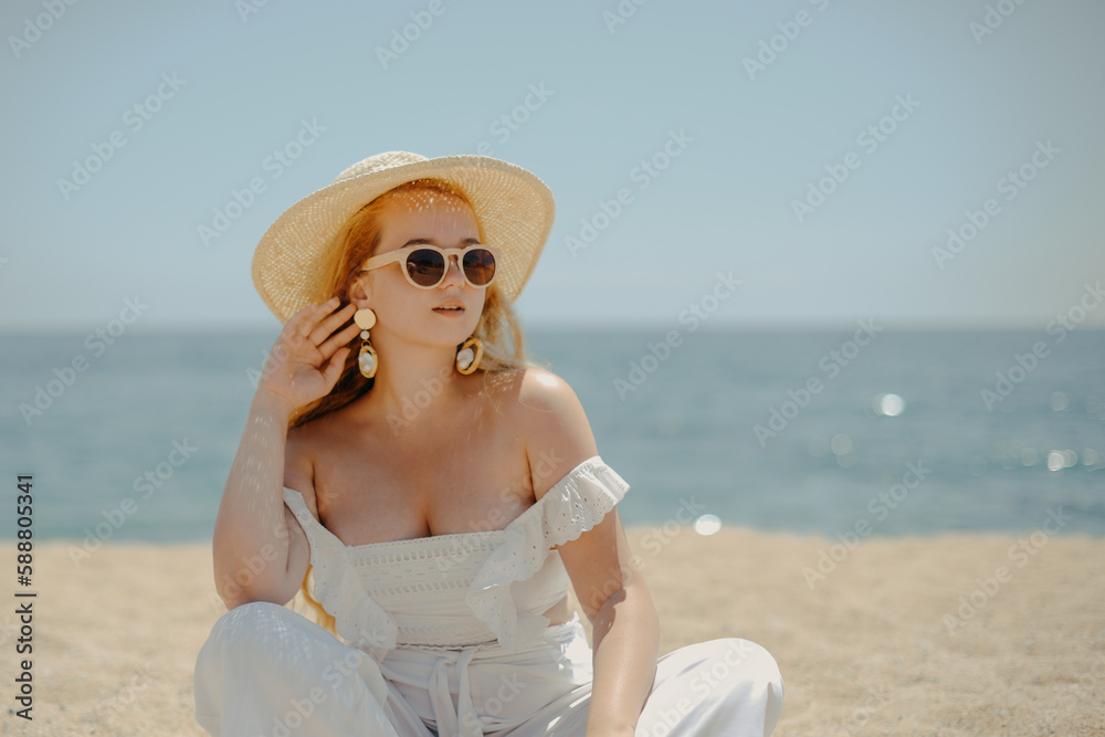Happy girl in white outfit sits on sand against the backdrop of the sea or ocean beach. Woman smiles and laughs, vacation and joy. Fashion model, beautiful jewelry, earrings, hat, sun glasses Happy girl in white outfit sits on sand against the backdrop of the sea or ocean beach. Woman smiles and laughs, vacation and joy. Fashion model, beautiful jewelry, earrings, hat, sun glasses