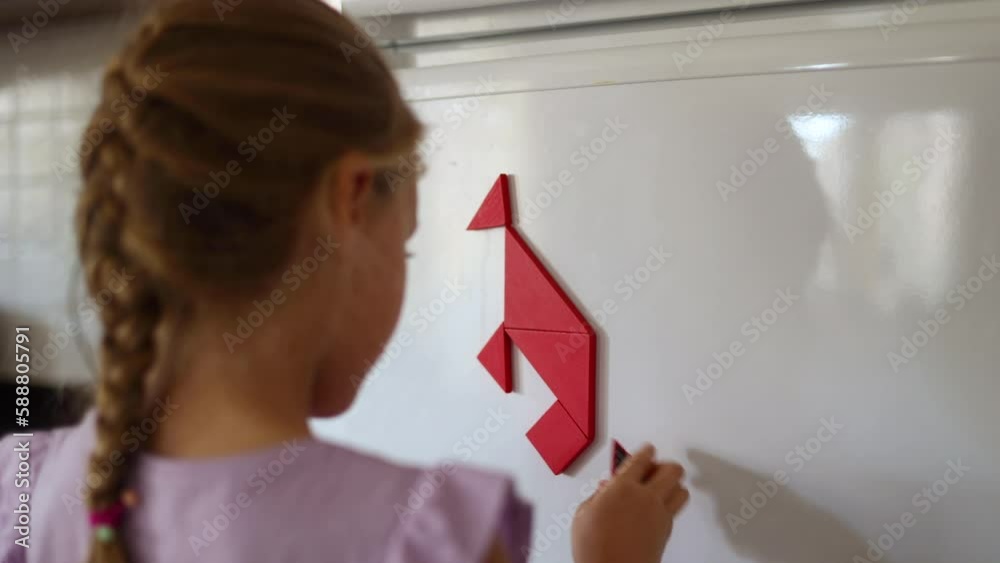 Close up of Cute little girl connecting pieces of tangram making kangaroo on a fridge, back view