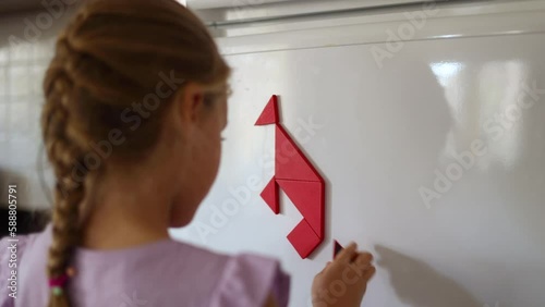Close up of Cute little girl connecting pieces of tangram making kangaroo on a fridge, back view