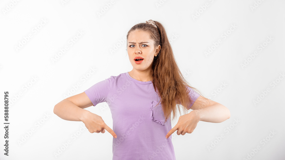 Portrait of confused young woman with long hair pointing finger down, frowns and looks puzzled, cant understand something, stands over white background Portrait of confused young woman with long hair pointing finger down, frowns and looks puzzled, cant understand something, stands over white background