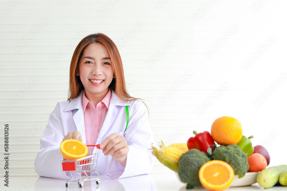 Portrait of a beautiful Asian nutritionist sitting on a white table with fruits and vegetables on the table. healthy food concept Portrait of a beautiful Asian nutritionist sitting on a white table with fruits and vegetables on the table. healthy food concept