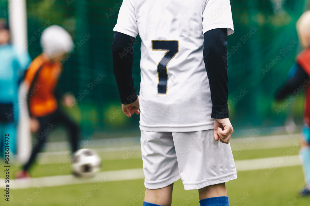 Fototapeta premium A young boy in a soccer team wearing a white jersey shirt with the number seven on its back. Youth football players playing tournament match