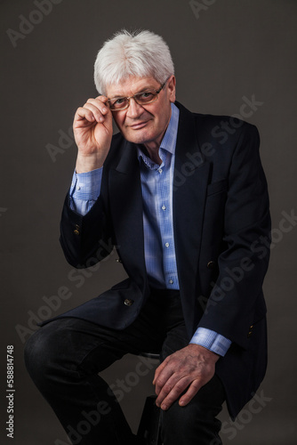 Portrait of an elderly man with glasses and a dark business suit on a dark background. 