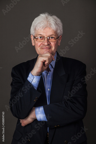 Portrait of an elderly man in glasses and a business suit on a dark background. 