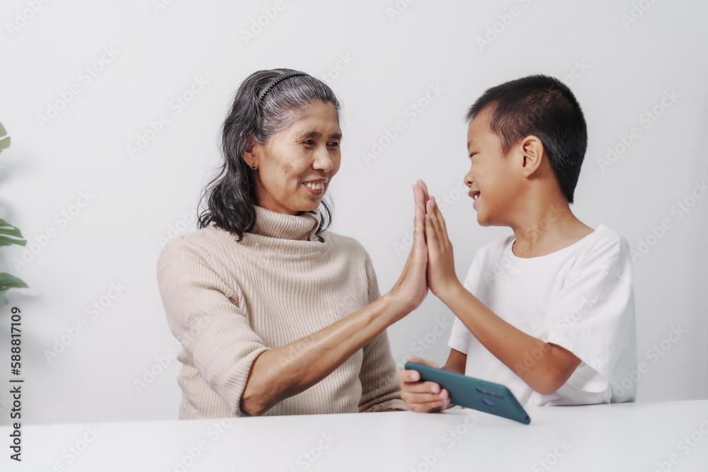 Getting hands high five after winning mobile game, Asian grandson and grandmother people sitting together at desk. Getting hands high five after winning mobile game, Asian grandson and grandmother people sitting together at desk.