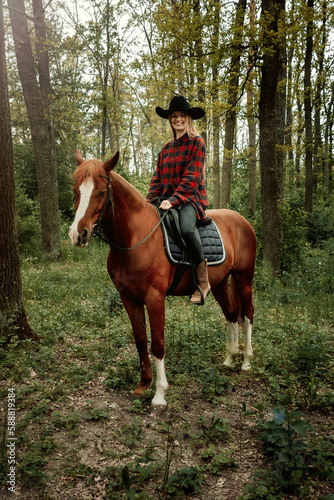 young and beautiful blonde woman with long hair in checked shirt sitting on a chestnut horse