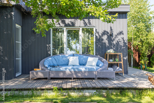 Fototapeta Naklejka Na Ścianę i Meble -  a large wicker sofa in fabric upholstery on a summer veranda outdoors in the sun against the backdrop of a country house and a large window
