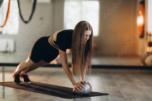 Full-length portrait of a beautiful smiling athletic woman in black and white tracksuit in a studio, working out with a ball. Flexible girl.