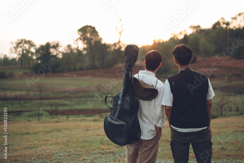 Two asian men close friends travelling together at campgrounds, enjoy camping amomg beautiful sunset time, Camping lifestyle outdoor and relax on summer. photo