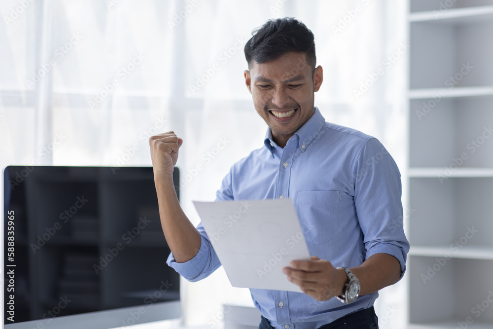Happy excited successful asian businessman triumphing in office, Portrait of a cheerful happy Asian business man  sitting at the laptop in office,