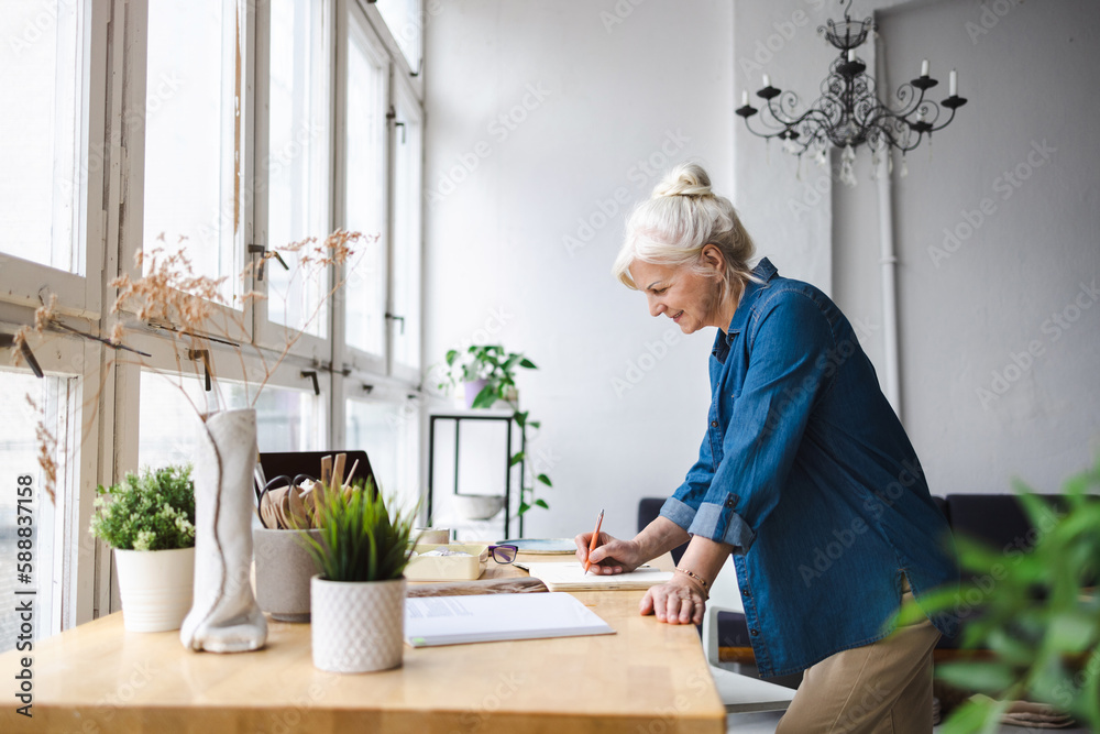 Smiling mature businesswoman writing in notebook while sitting at table in office Smiling mature businesswoman writing in notebook while sitting at table in office