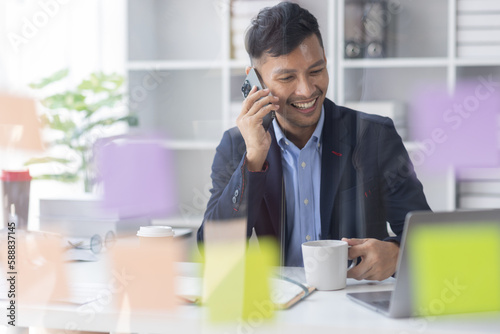 Cheerful business Asian man freelancer making telephone call share good news about project working in office workplace, Asian business man planning finance concept.