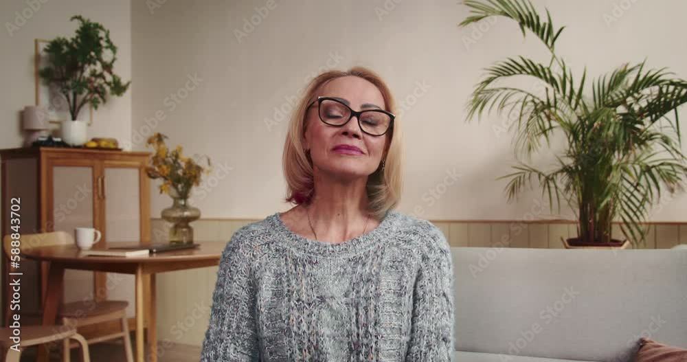 Portrait of beautiful happy senior 60s Caucasian woman adjusting stylish eyeglasses looking at camera at cozy home.