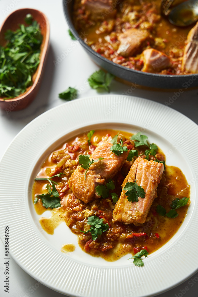 Red Salmon Curry with Tomatoes and Fried Vegetables with a Garnish of Cilantro. Asian Cuisine. Fried salmon with vegetables and green cilantro in white plate. Close up. Vertical photo Red Salmon Curry with Tomatoes and Fried Vegetables with a Garnish of Cilantro. Asian Cuisine. Fried salmon with vegetables and green cilantro in white plate. Close up. Vertical photo