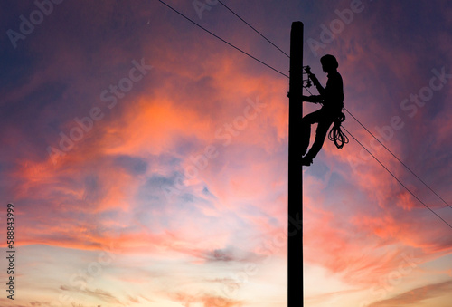 Silhouette of Electrician repairing wire on electric power pole at the sunsetbackground.