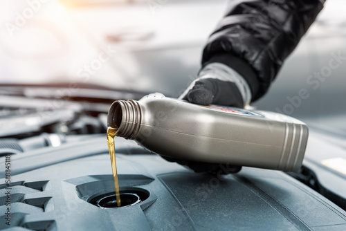Close-up driver hand holding small bottle can pouring synthetic motor oil in diesel or petrol turbocharged vehicle engine due oil consumption. New lubricant diy change. Car service maintenance work