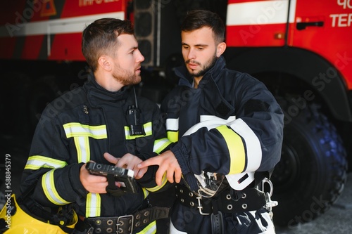 Portrait of two firefighters in fire fighting operation, fireman in protective clothing and helmet using tablet computer in action fighting