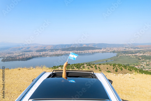 Woman holding Argentina flag from the open car sunroof,  window driving along the serpentine road in the mountains. Top view. Concept © flowertiare