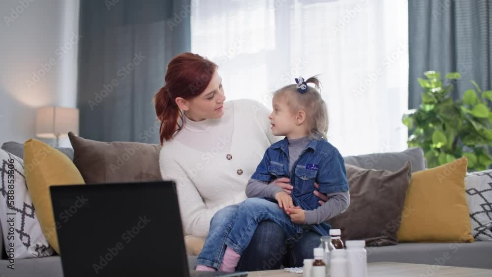caring woman with a small female child in arms treats daughter for cold and shows her runny nose spray sitting on couch in room caring woman with a small female child in arms treats daughter for cold and shows her runny nose spray sitting on couch in room
