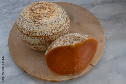 Paris, France - 03 24 2023: French culinary Still Life. Piece of cheese Mimolette placed on a wooden pan. photo